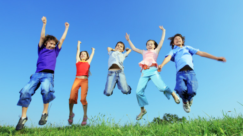 Group of five happy children jumping on meadow.